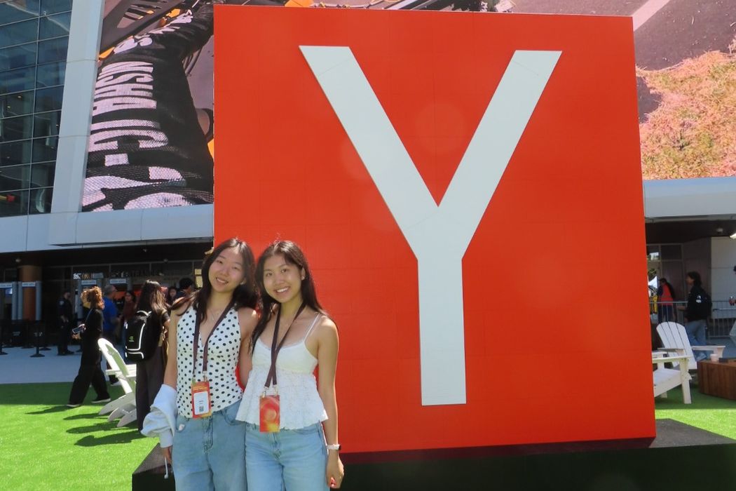Two attendees with lanyards smile in front of a giant red Y block on a green lawn
